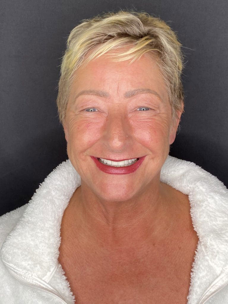 A smiling woman with short hair, wearing a white top and a jacket with a fur-lined collar.