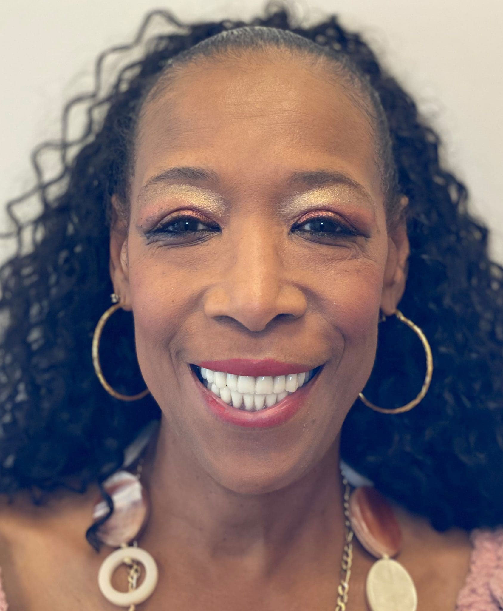 A smiling woman with long hair, wearing a pink top and large hoop earrings.