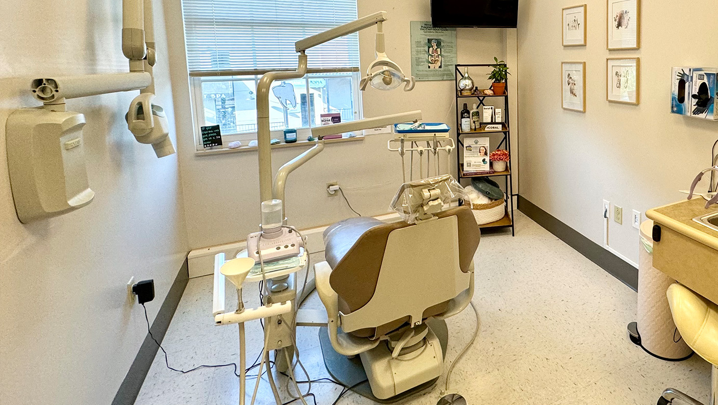 The image shows a dental office interior with various pieces of equipment and furniture, including dental chairs, a counter with multiple sinks, a reception area with a desk and chair, and a large window.