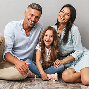A family of four, with a man, woman, and child sitting on the floor, posing for a photo with smiles.