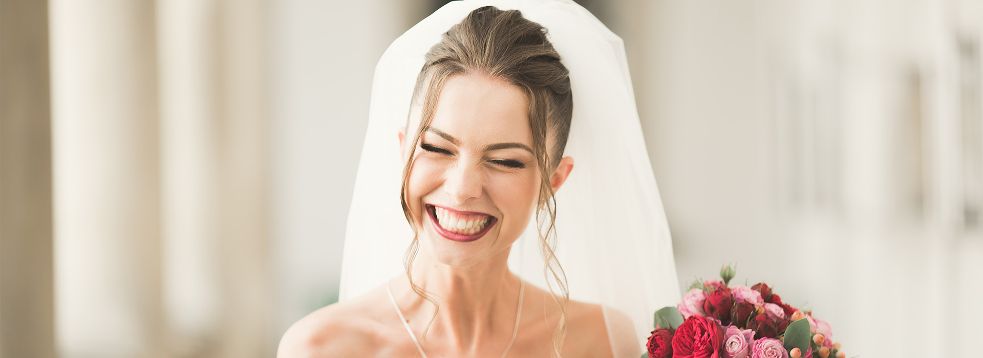 The image is a photograph of a woman wearing a white wedding dress and holding a bouquet, smiling at the camera.