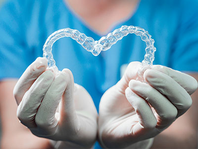 A dental professional s hands gently cradling a transparent heart-shaped dental appliance, symbolizing care and compassion in the field of dentistry.