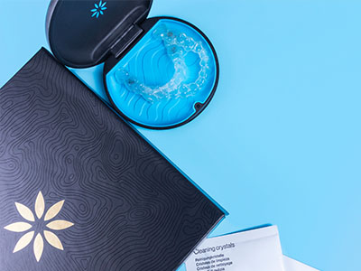 The image displays a dental impression tray with a toothpaste tube and a box of cleaning crystals in the background, all set against a blue backdrop.