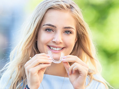 Smiling woman holding a clear aligner tray, showcasing her oral care routine.