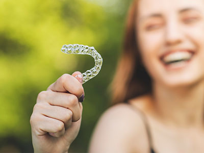 A young woman holding a transparent plastic aligner, smiling and laughing.