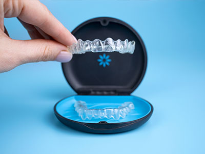 The image shows a person s hand holding an open box containing a set of clear aligners, which are used for teeth straightening.