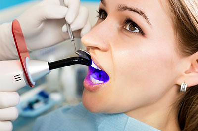 A woman receiving dental care, with a dentist using a device to examine her teeth.