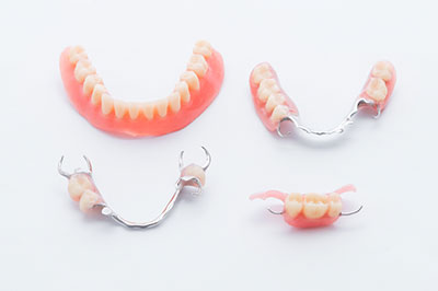 The image displays a collection of three dental retainers with toothpicks, each featuring an upper and lower set of teeth in various states of wear or replacement.