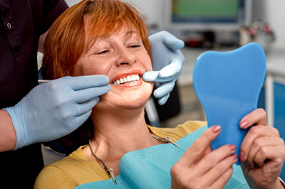 A woman in a dental chair receiving dental care, smiling and showing off her teeth.