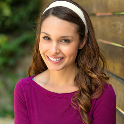 A young woman with long hair, wearing a purple top and a light blue headband, smiling at the camera.