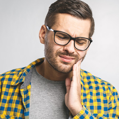 Man with glasses and beard, holding his hand to his mouth and showing a toothache expression.