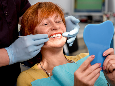 A woman in a dental chair receiving teeth whitening treatment, with a blue plastic mouthguard and a dental hygienist applying it.