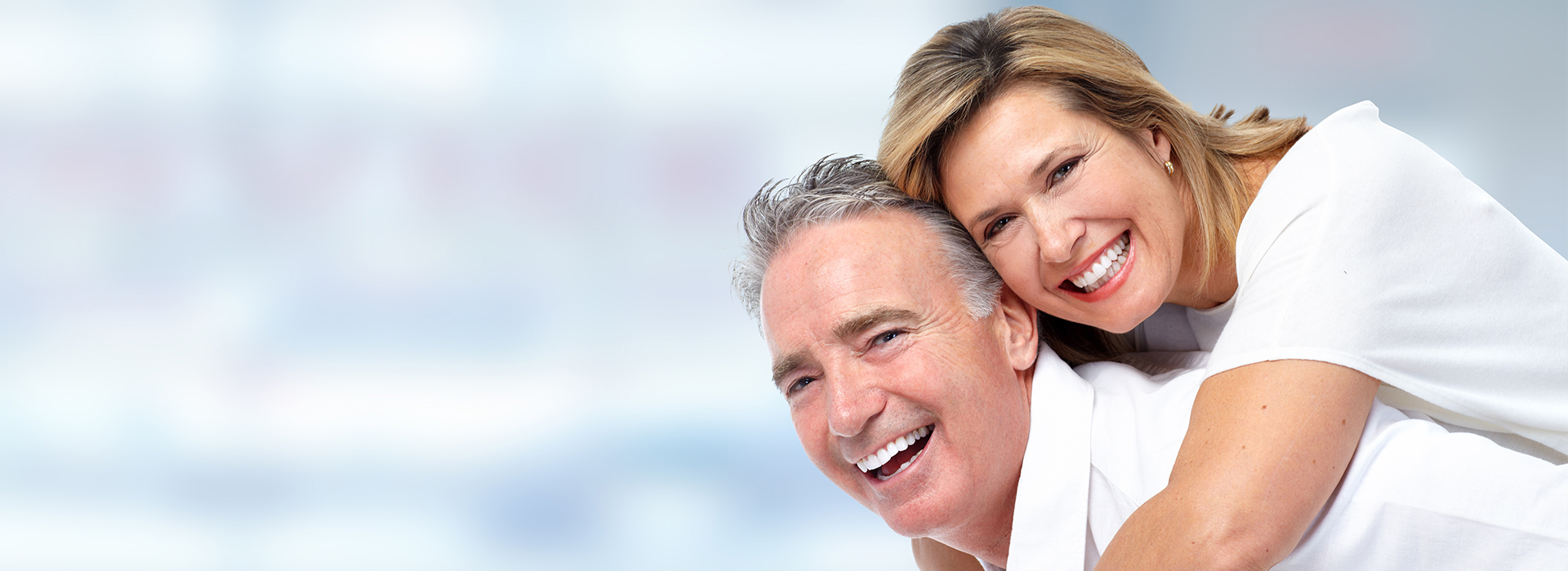 A man and a woman smiling together, with the man wearing a white shirt and the woman in a light-colored top.