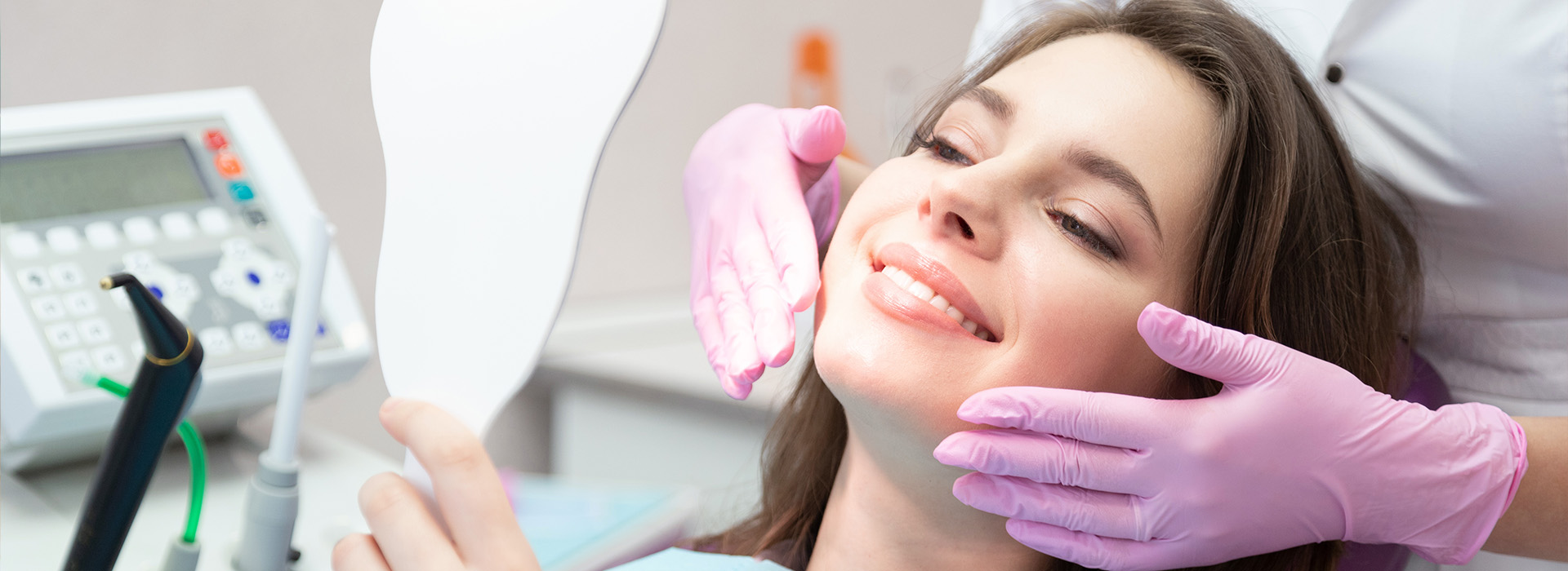 A woman receiving dental treatment with a dental hygienist using a mirror to inspect her teeth.