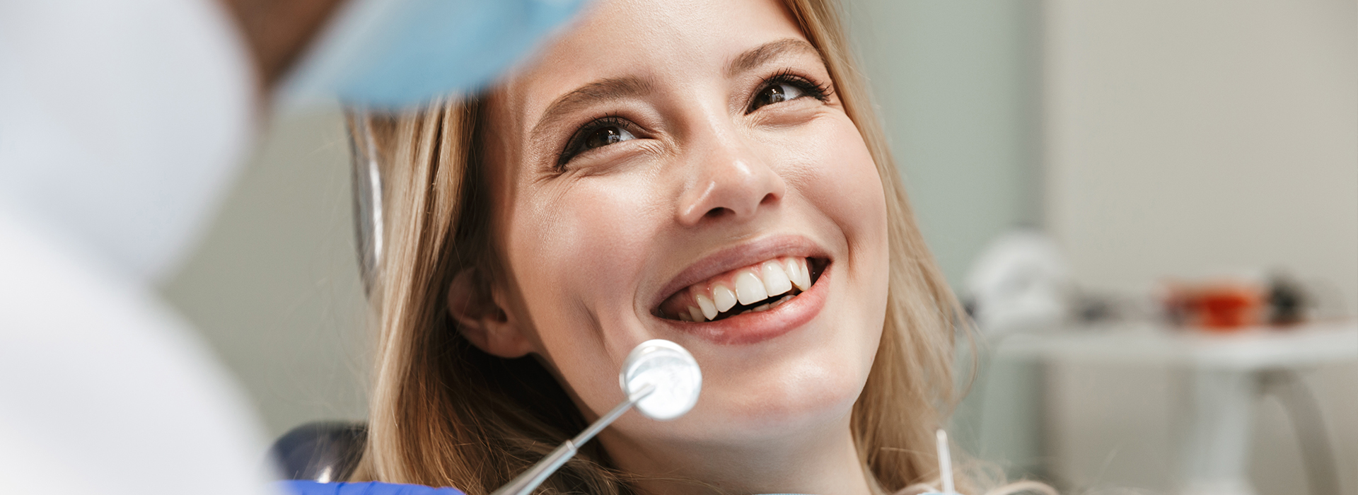 A smiling woman in a dental chair, being attended to by a dentist.