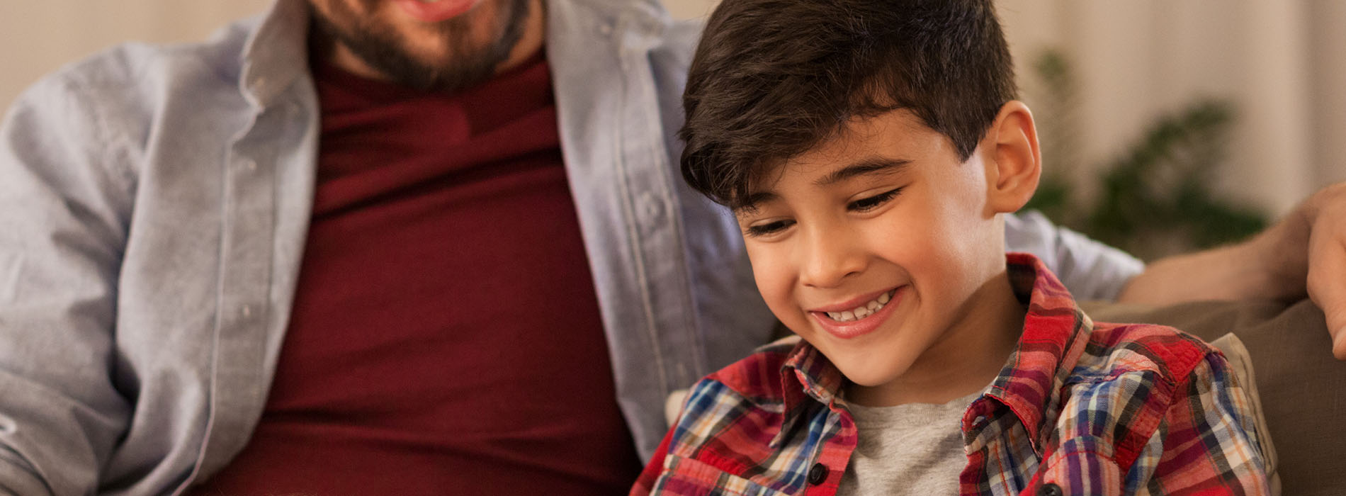 The image shows a man and a child sitting together on a couch, smiling at the camera.