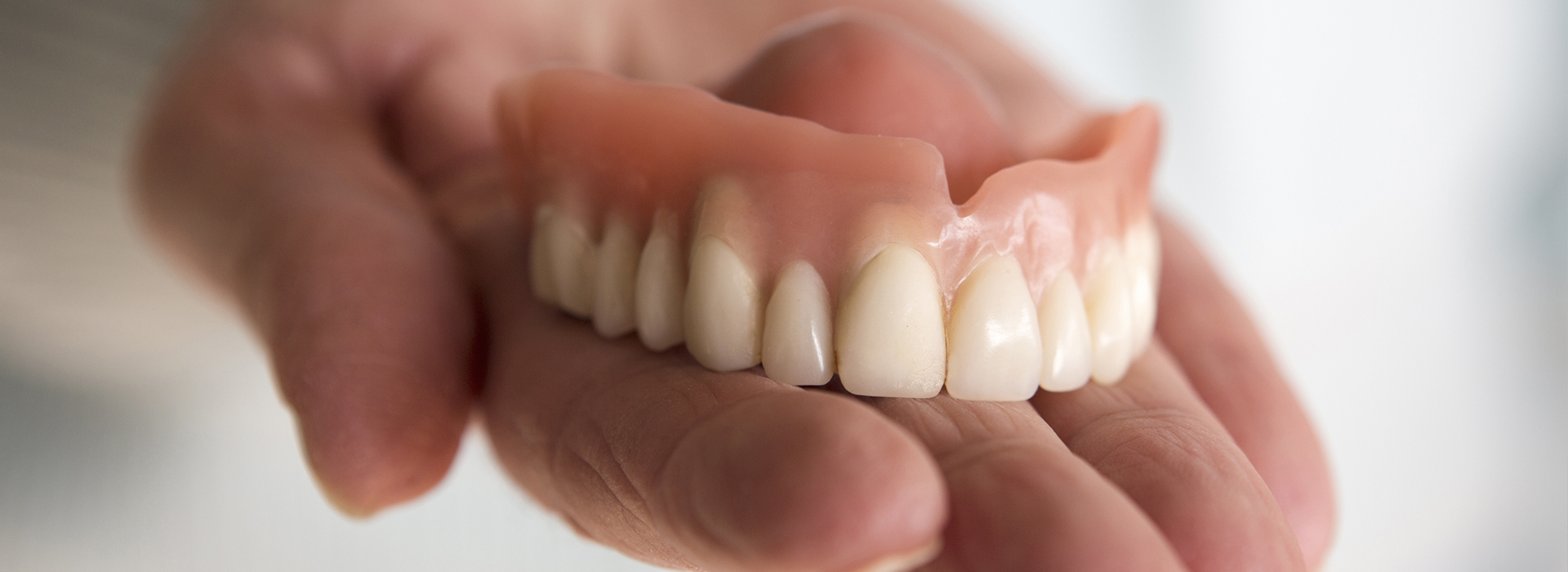 The image shows a person holding a set of dentures, which are white and appear to be made of porcelain or acrylic.