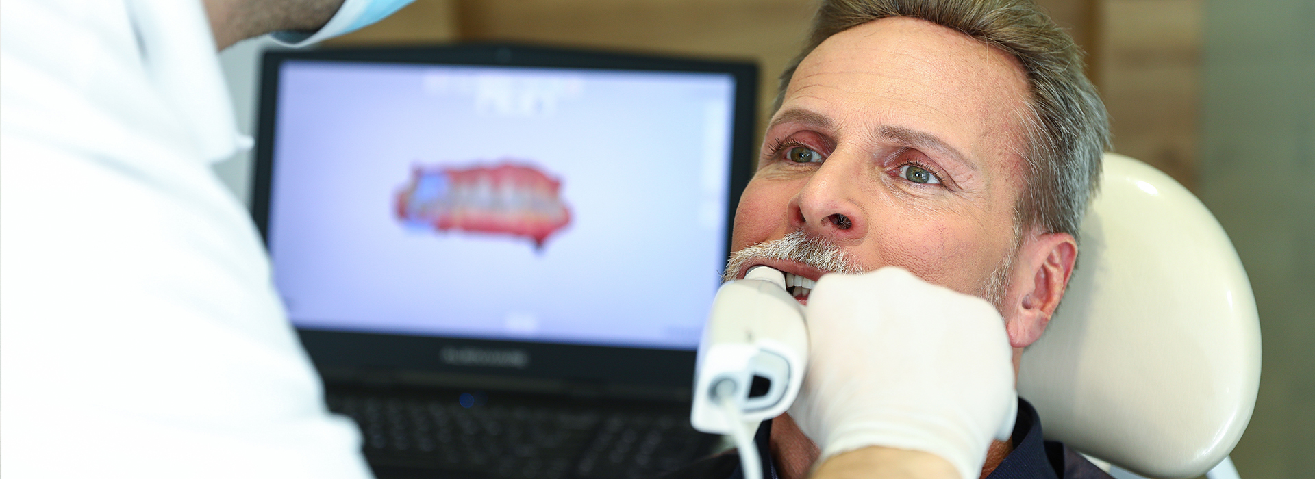 This is an image of a man receiving dental treatment, with a dentist performing the procedure using specialized equipment.