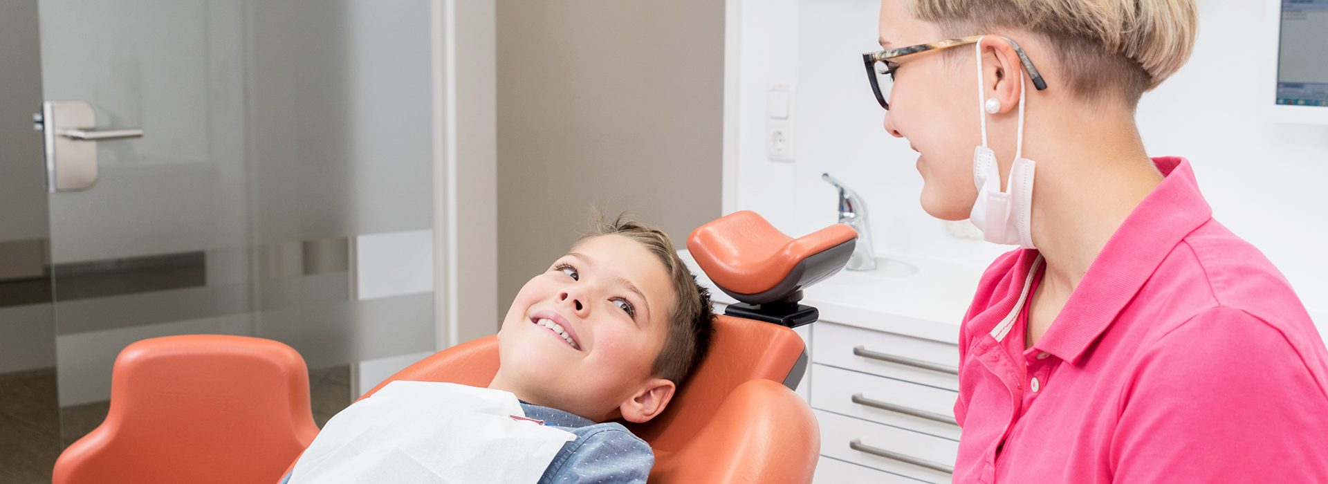 A dental office scene with a dentist and patient, featuring a young child in a chair.