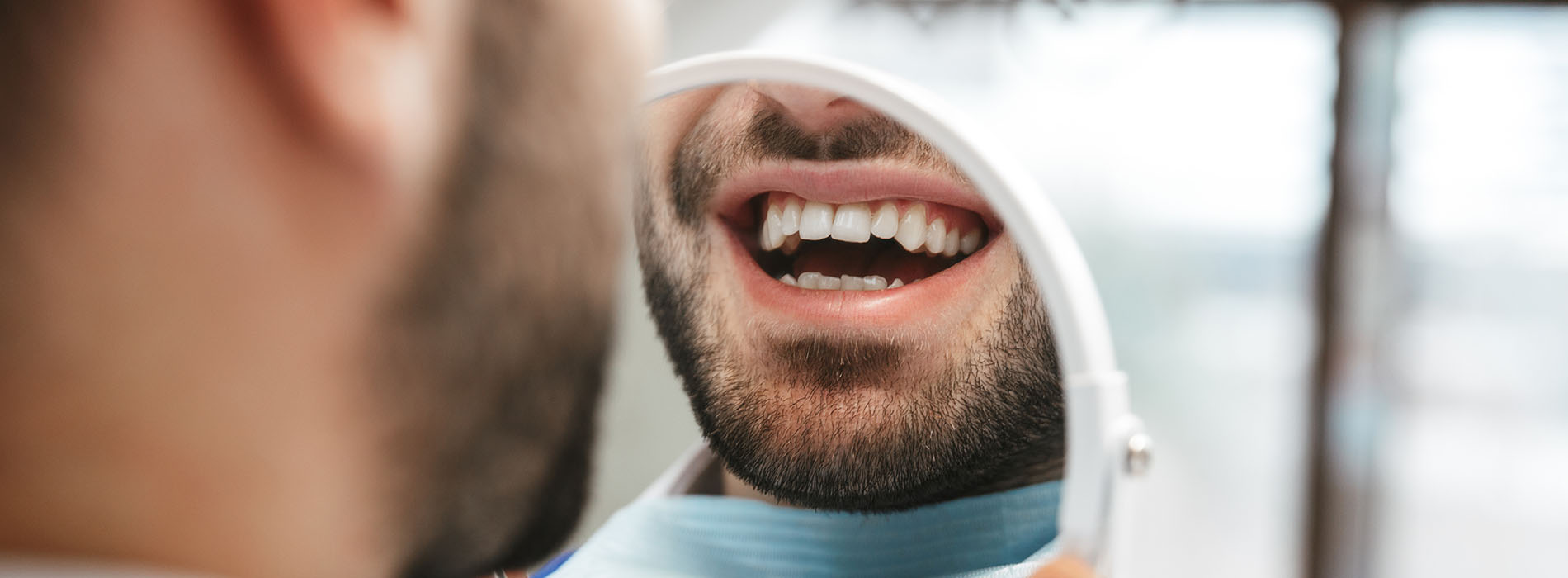 An image featuring a man with a beard and mustache, holding an open mouth, possibly in conversation or laughter, with a blurred background that suggests an indoor setting.