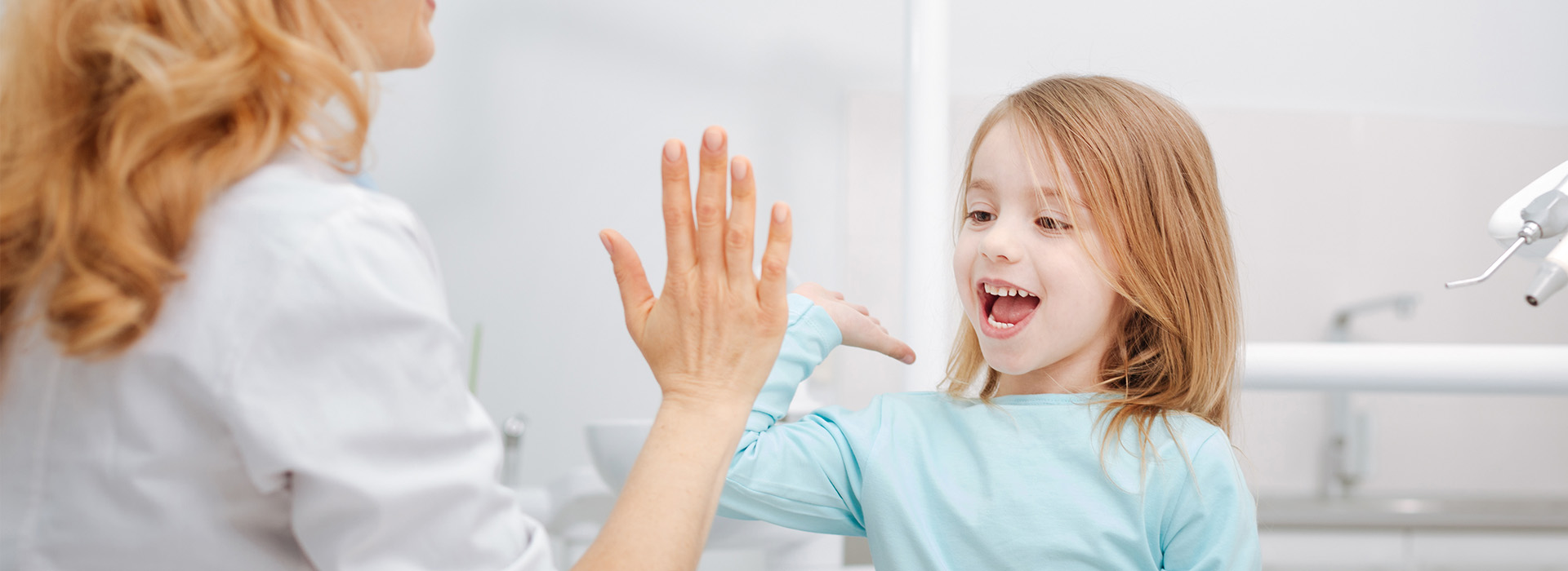 A young girl with a toothbrush in her mouth, receiving a high-five from an adult, possibly during a dental visit.