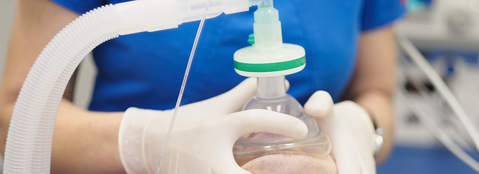 A person in a white lab coat holding a clear plastic bag with a green cap, containing a liquid, possibly for medical use or research.