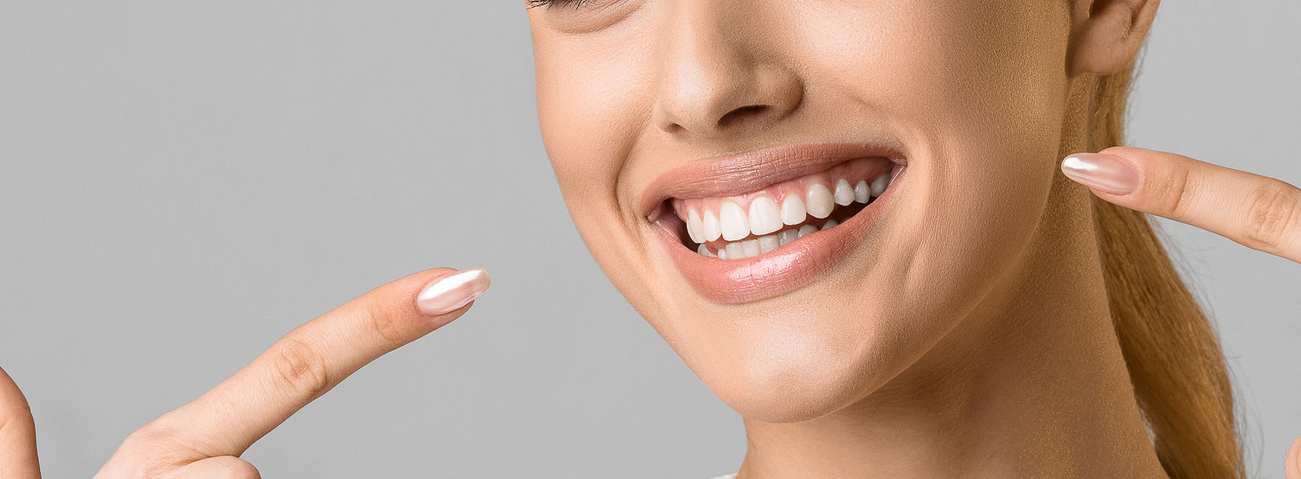 A woman with a radiant smile, showcasing her teeth and holding up two fingers near her face.