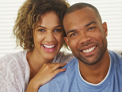 The image shows a man and woman posing together, smiling at the camera.