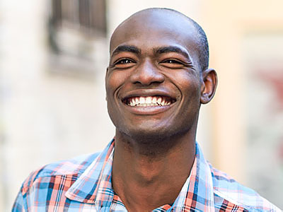 A smiling man with a shaved head, wearing a plaid shirt and standing outdoors.