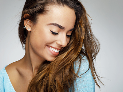 The image is a close-up portrait of a woman with long hair, smiling and looking slightly away from the camera.