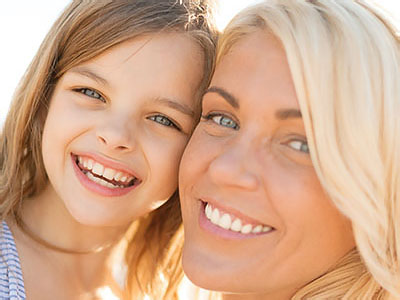 A woman and a young girl smiling at the camera, with the woman s face partially obscured by a filter.