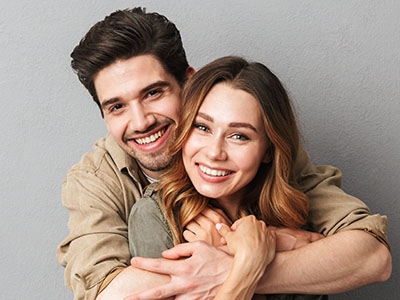 The image depicts a man and woman embracing each other, both smiling, with the woman wearing a necklace. They appear to be in a warm, affectionate pose.