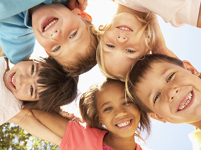 A group of children, possibly siblings, smiling and posing together for a photo in bright sunlight.