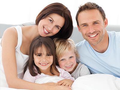 A family of four, including a man and woman with two children, posing together in a bedroom setting.